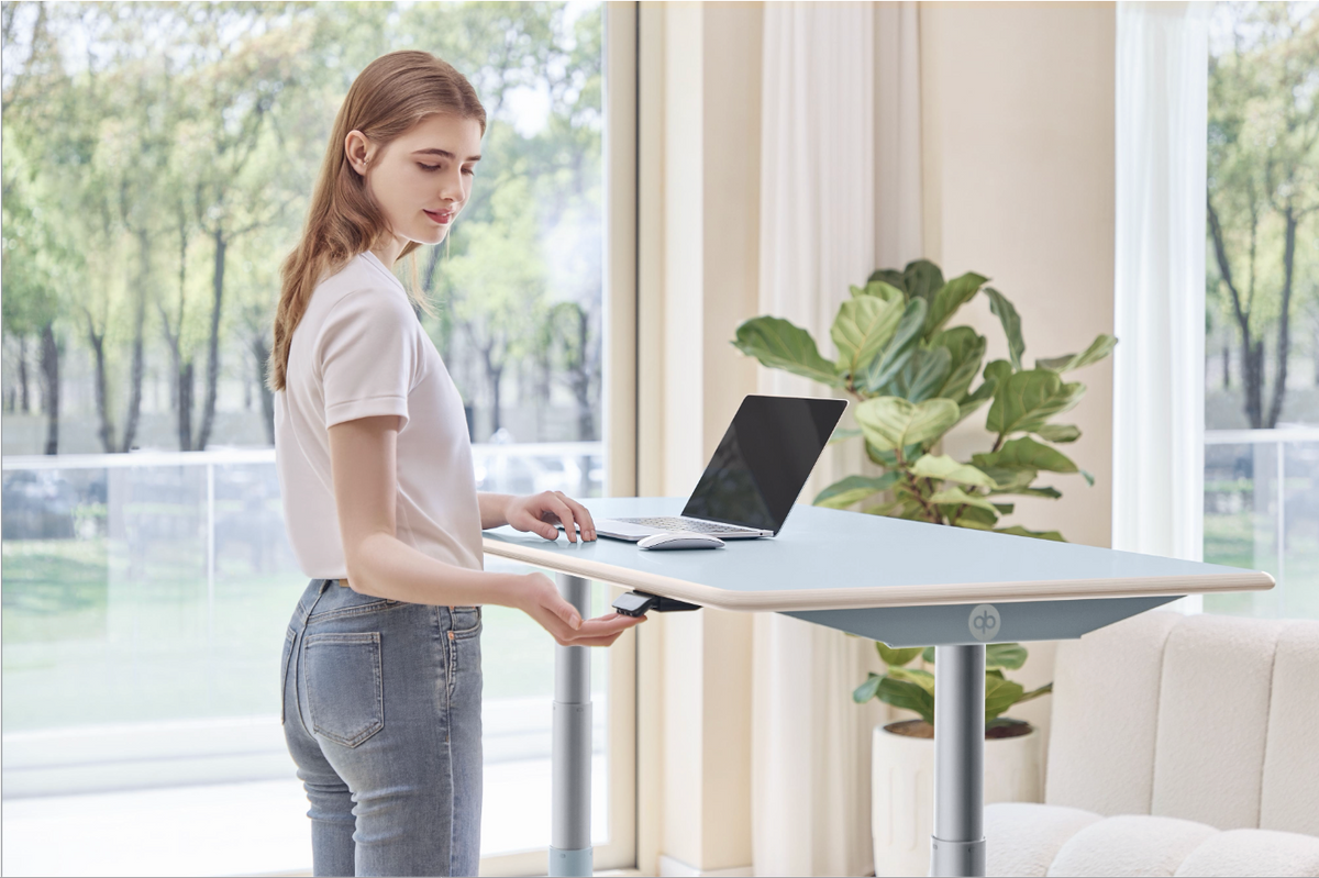 Woman adjusting the Clear Sky Blue Ease Standing Desk at standing height