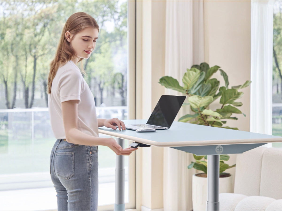 Woman adjusting the Clear Sky Blue Ease Standing Desk at standing height