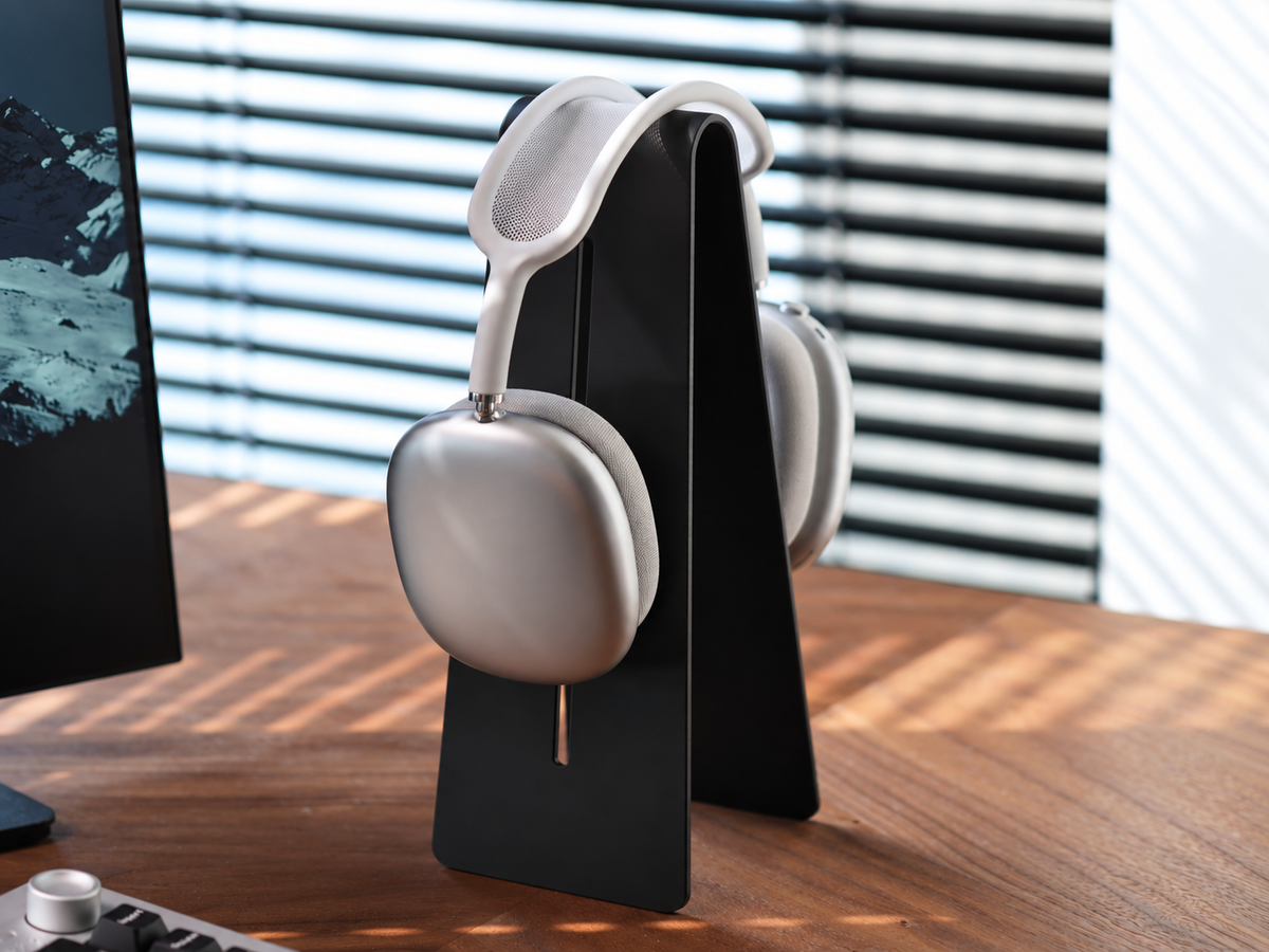 Black aluminum headphone stand holding silver over-ear headphones in a desk setup