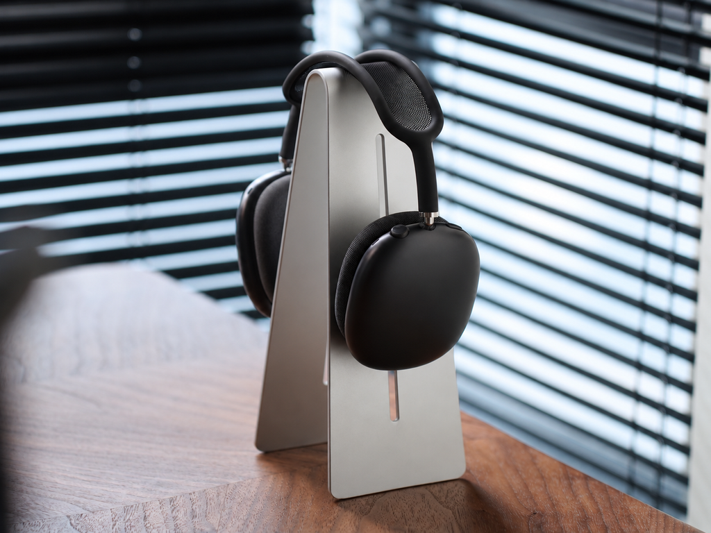 Silver aluminum headphone stand holding black over-ear headphones on a walnut desk