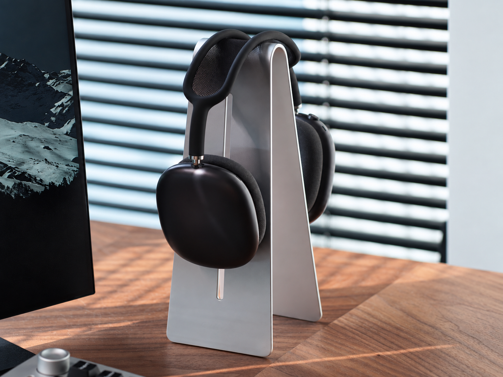 Silver aluminum headphone stand holding black headphones beside a monitor