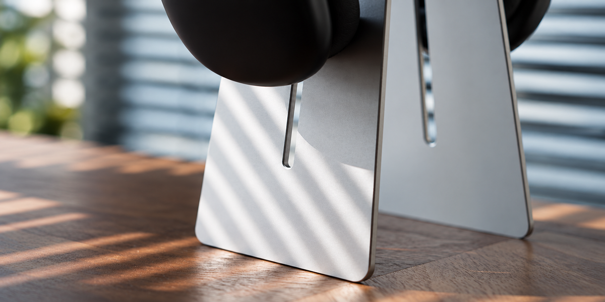 Aluminum headphone stand holding headphones on a sunlit wood desk